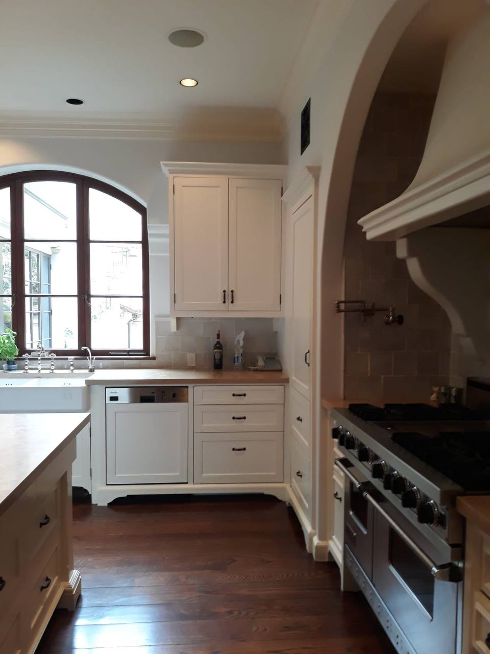 Custom cream shaker kitchen cabinets with butcher block counters and arched plaster range hood in Glendale CA