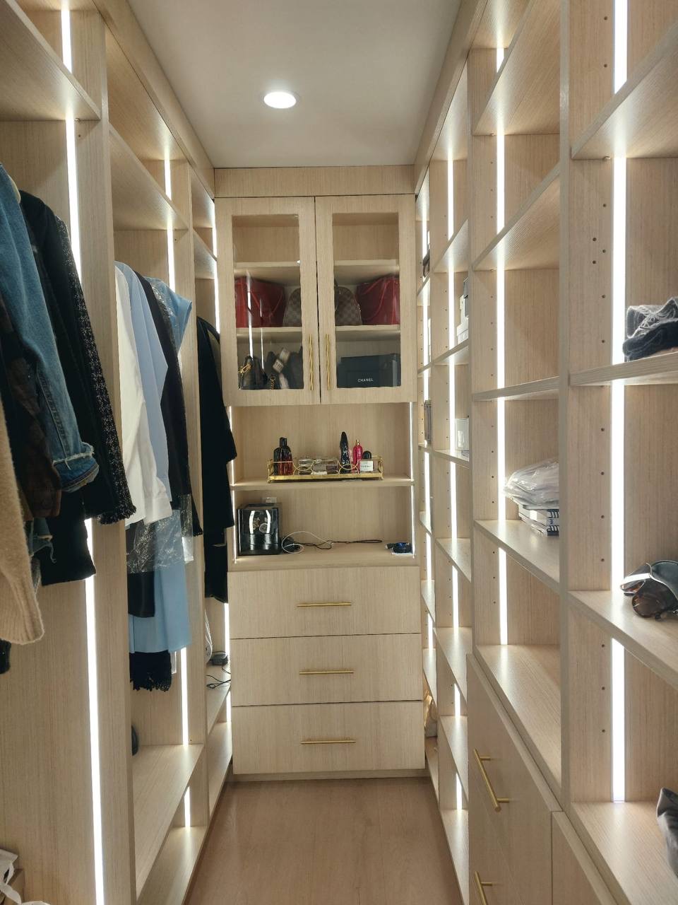Custom white oak walk-in closet with LED-lit shelving and glass display cabinets in Glendale CA
