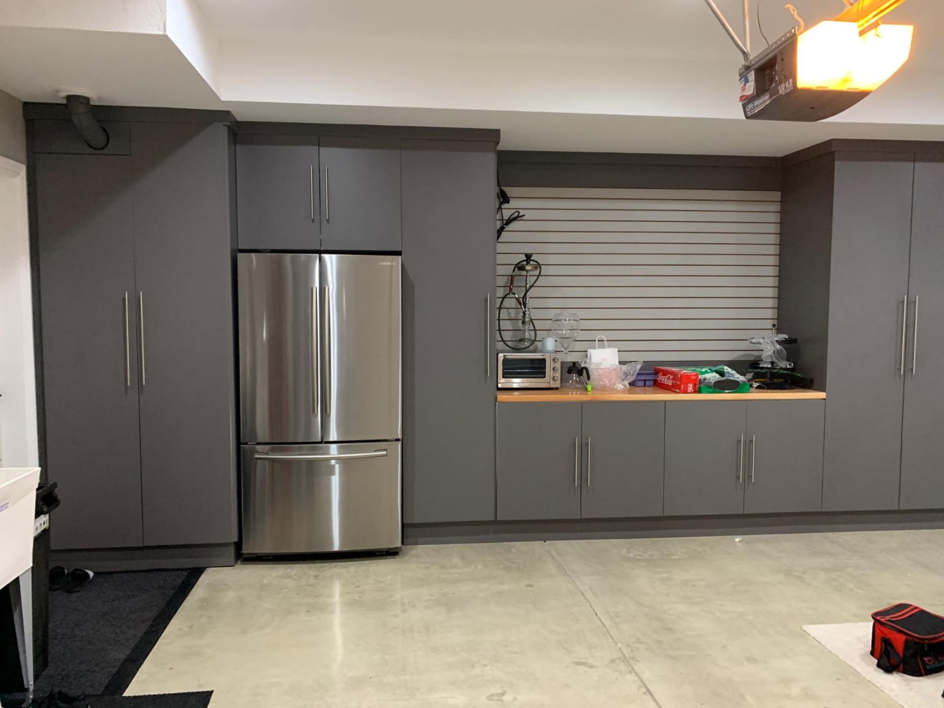 Custom full-height gray garage cabinets with stainless French-door fridge, butcher-block workbench and slat-wall storage in Los Angeles