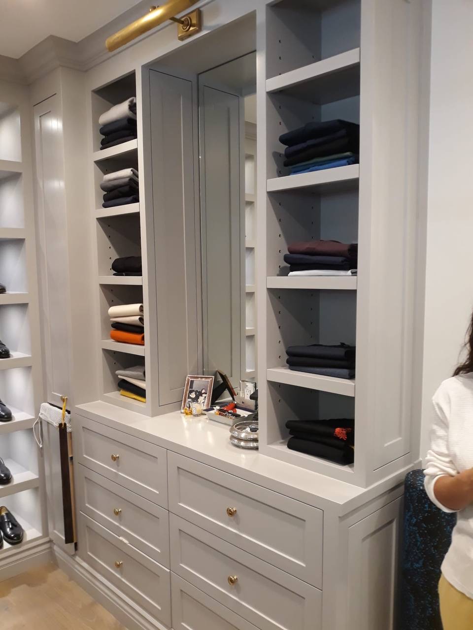 Custom gray walk-in closet with built-in shelving, drawer bank, and brass picture light in Glendale CA